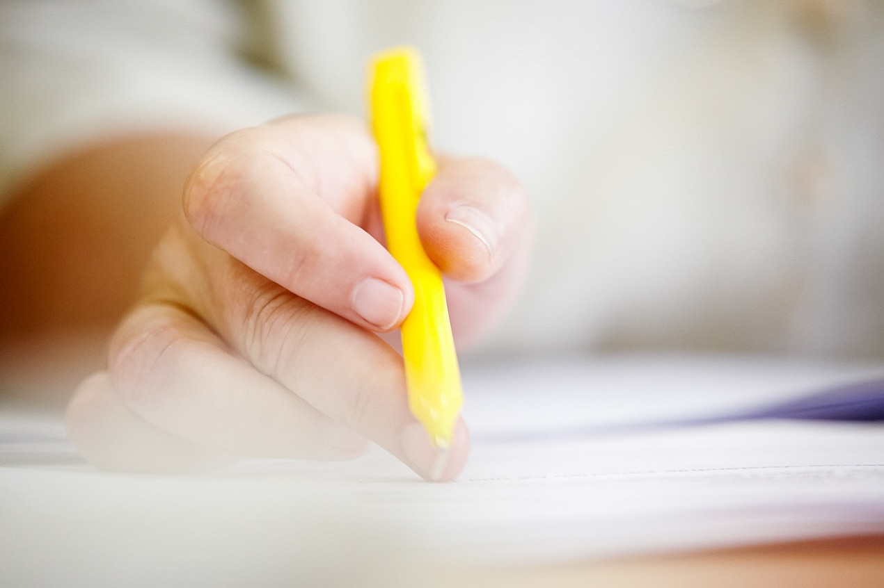 schreibende Hand in Detailansicht ist zu sehen mit gelbem Stift in der Hand auf weißem Papier- Pressefrauen Frankfurt schreiben und texten für PR